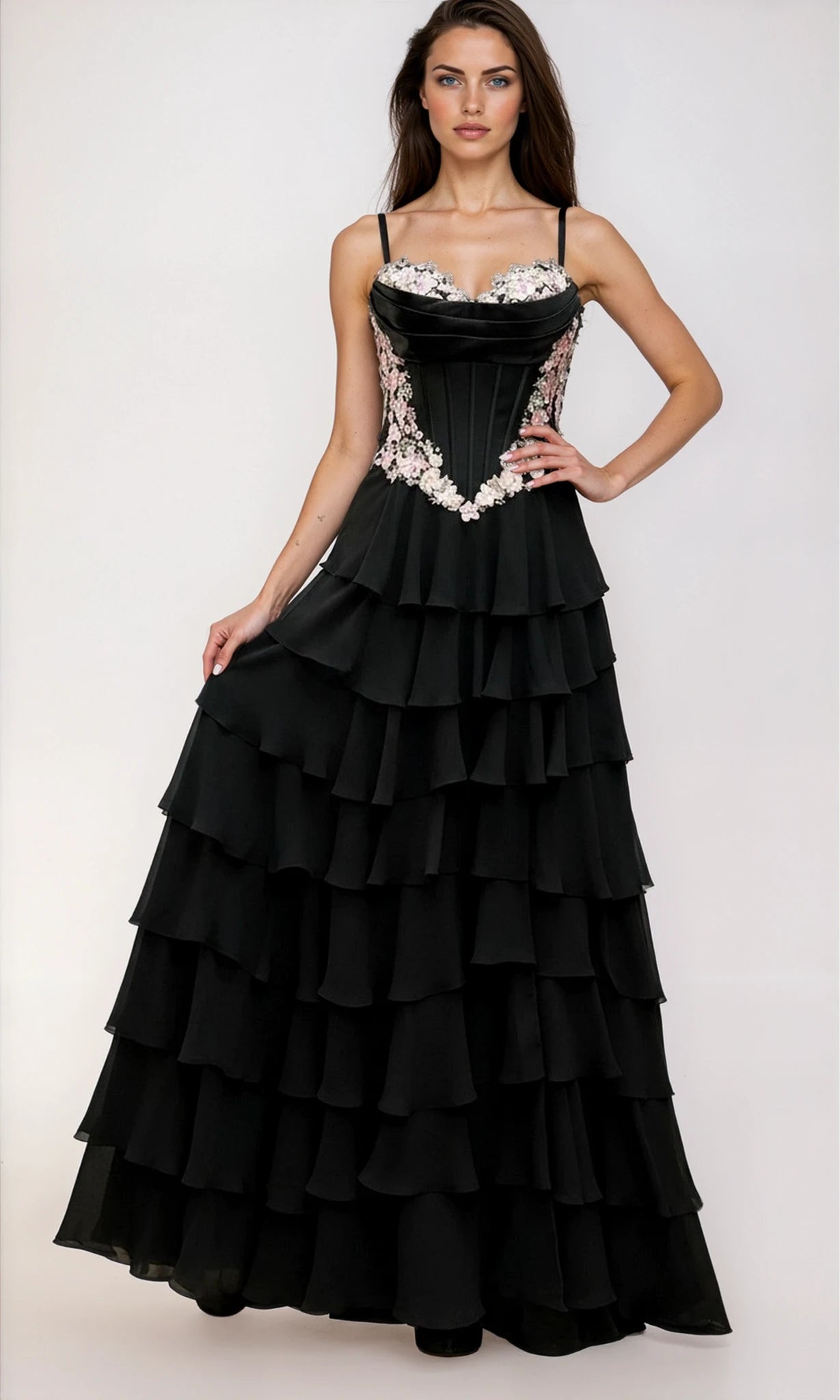 A woman stands against a plain light background, wearing the Dave & Johnny 12966 Long Tiered A-Line Prom Dress—a black gown with thin straps and floral embroidery on the bodice.